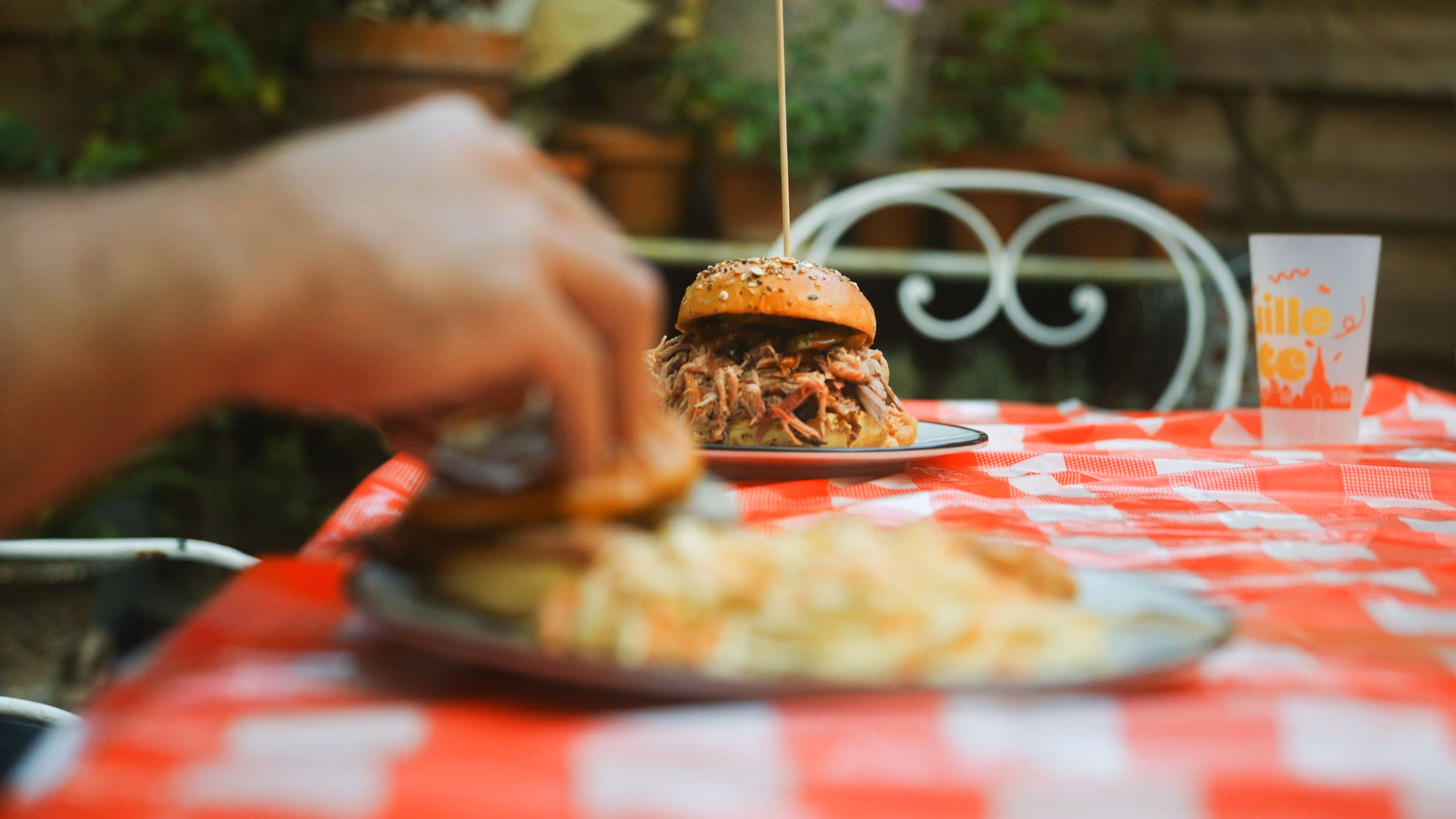 Burger au pulled pork fumé servi en extérieur, sur nappe vichy rouge
