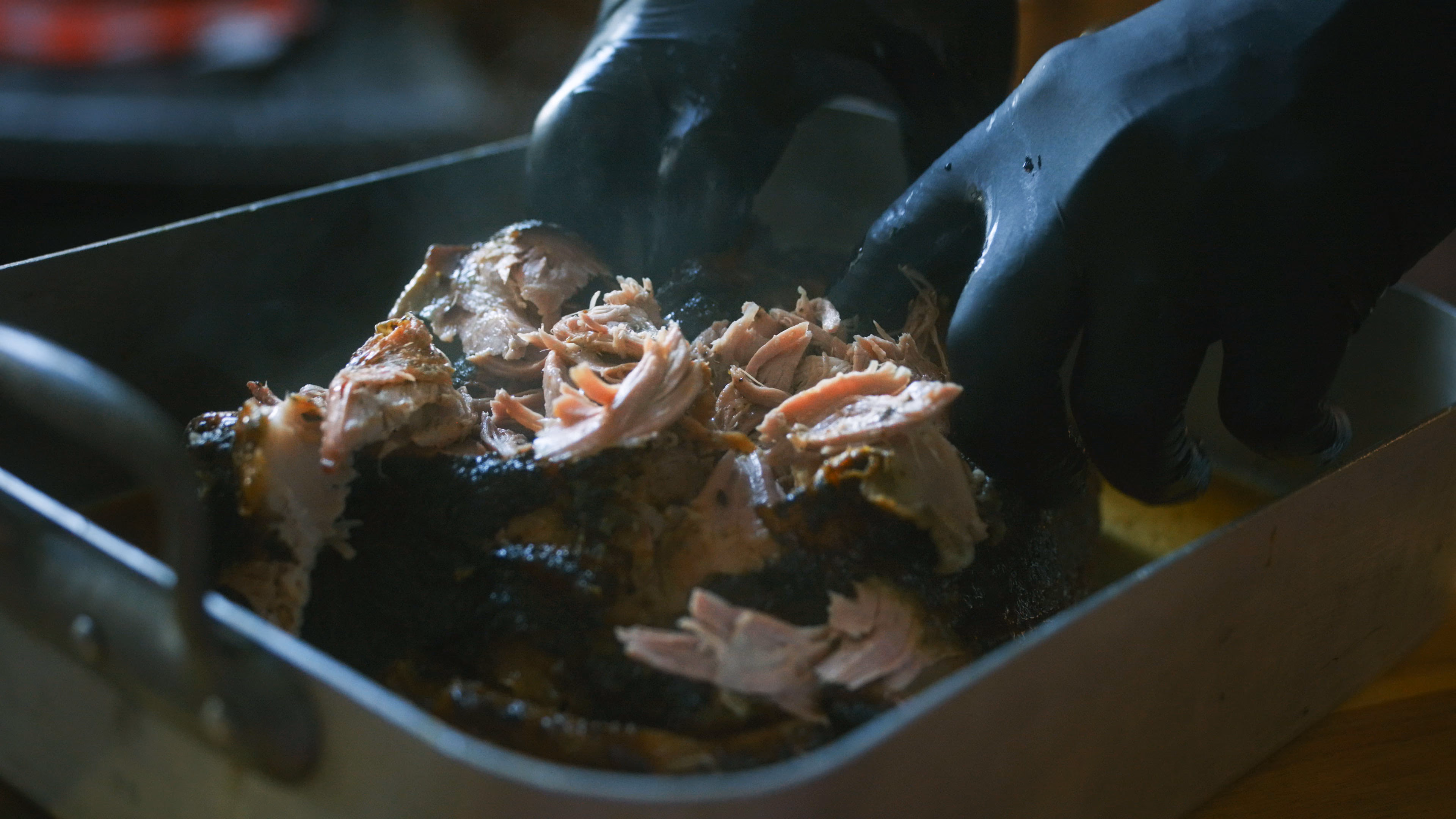 Pulled pork effiloché à la main, gants noirs, à la sortie du fumoir
