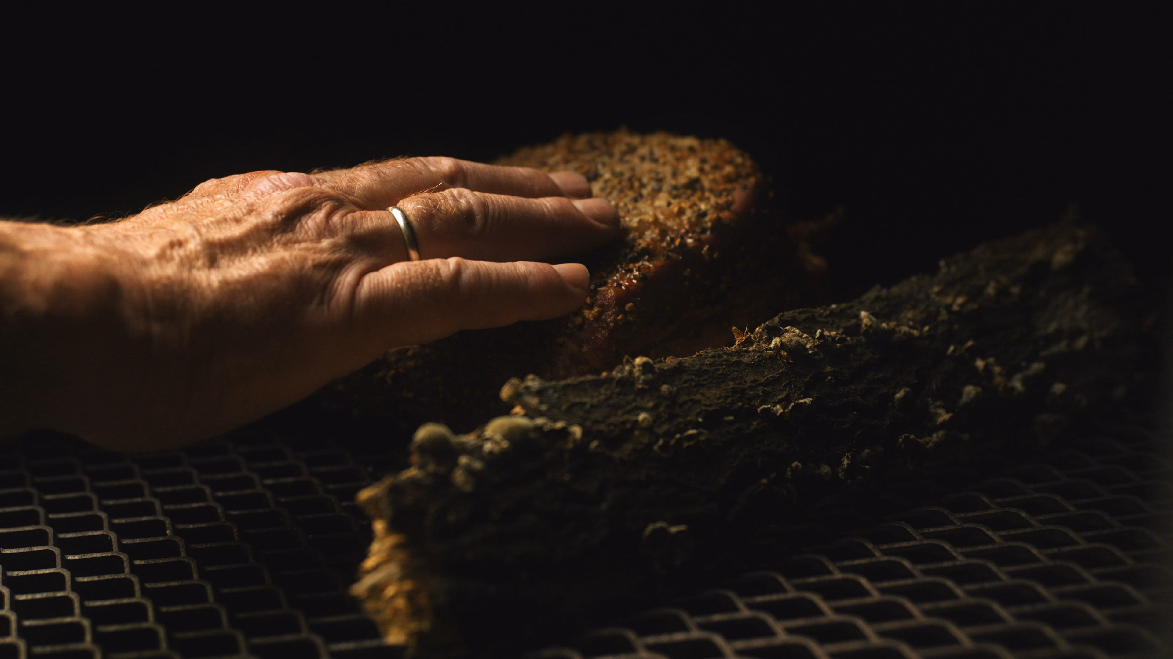 Main saisissant un brisket au bark sombre posé sur la grille du smoker