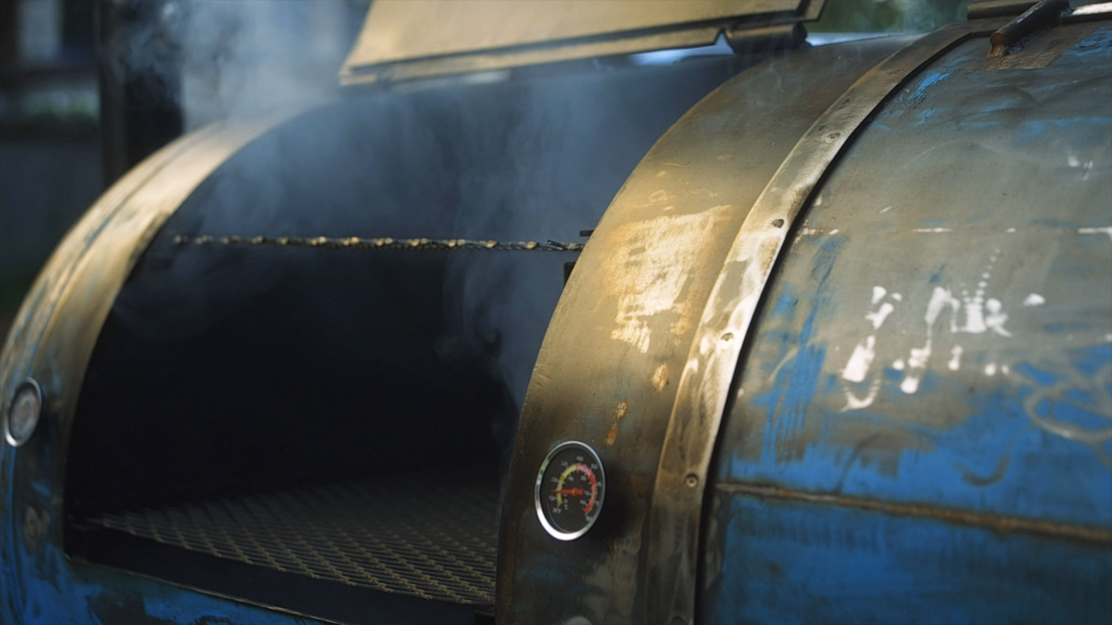 Smoker offset bleu, couvercle ouvert, fumée qui s’échappe de la chambre de cuisson