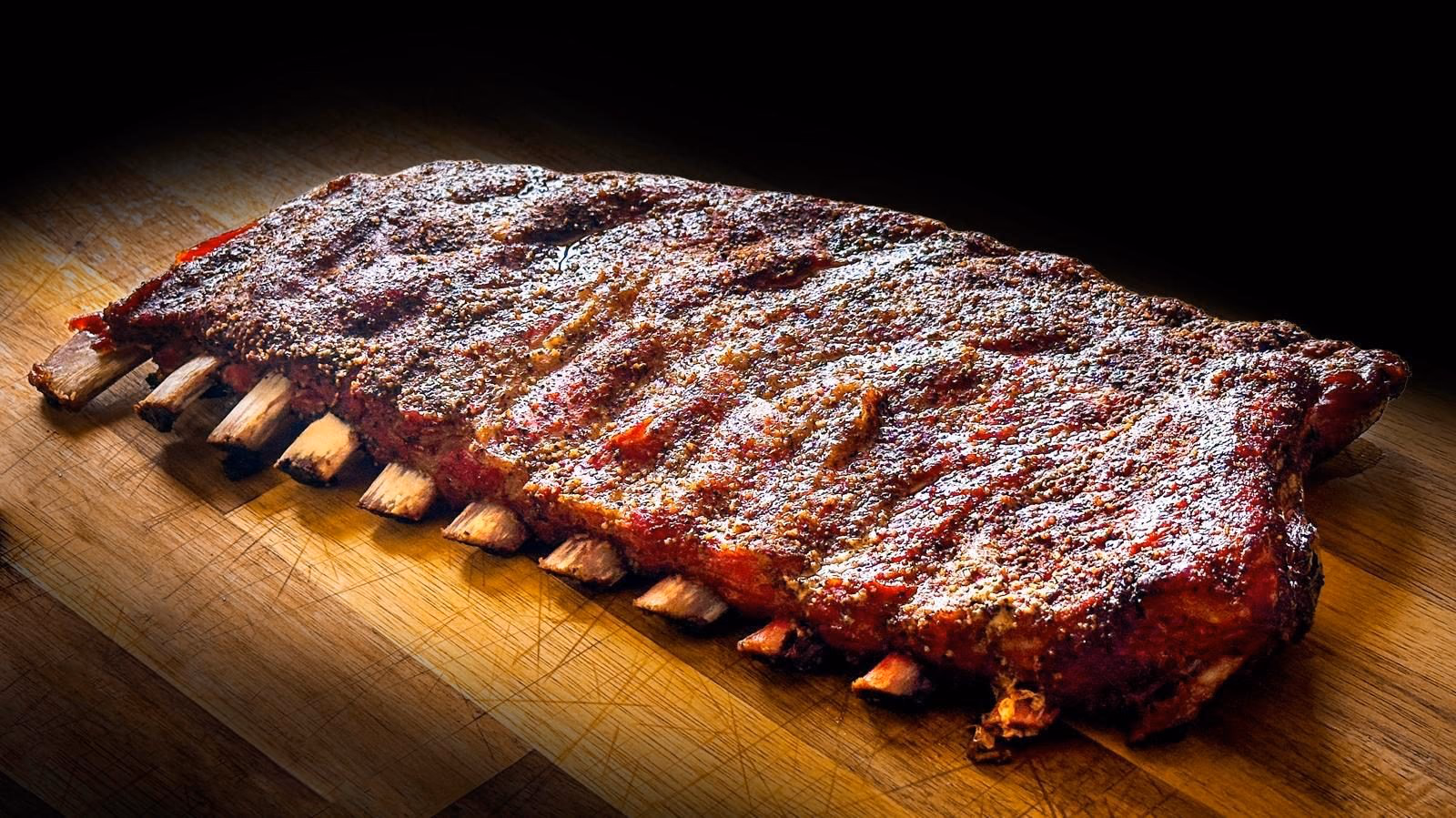 Rack entier de ribs de porc fumés au bois, croûte d’épices caramélisée sur planche